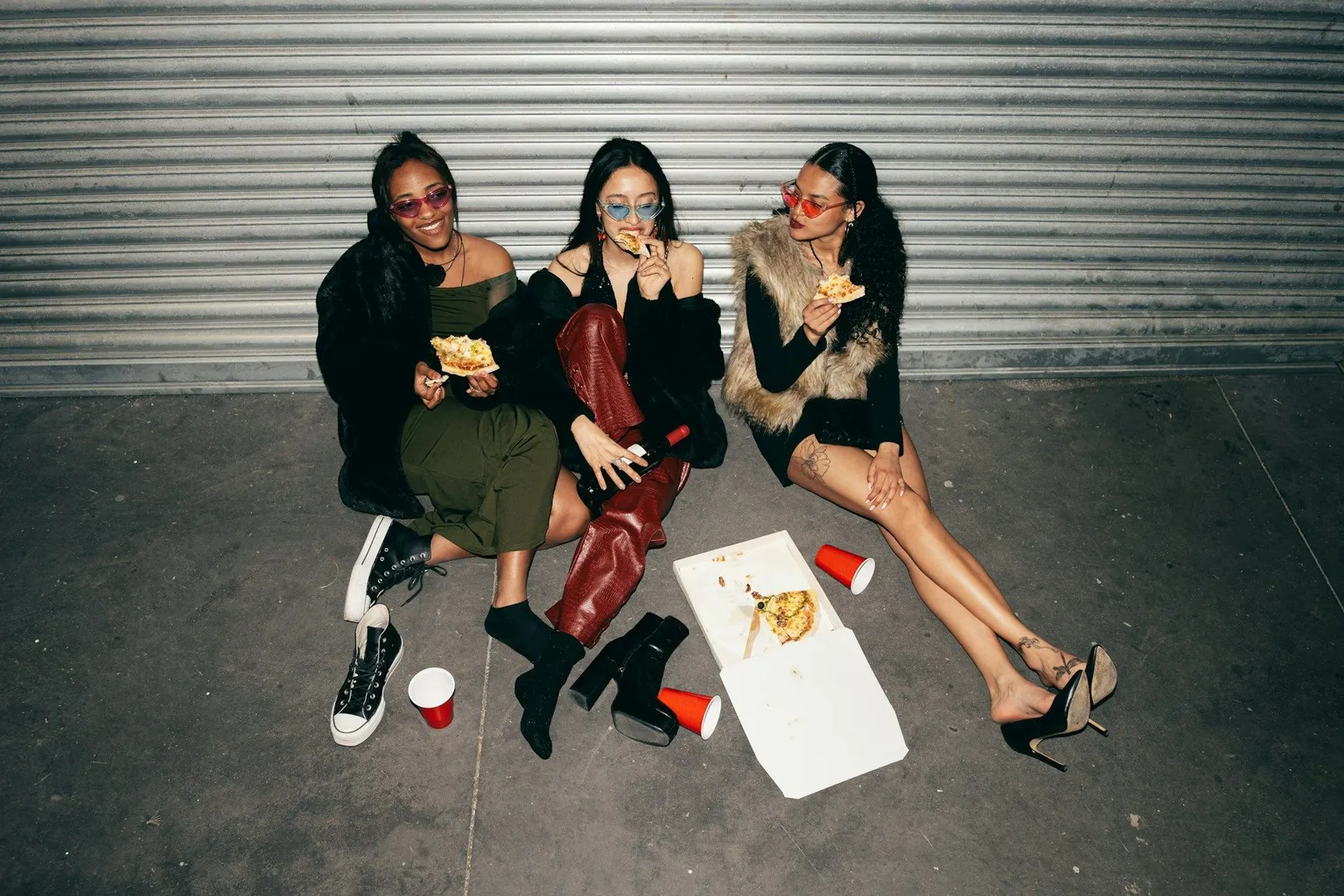 Three young women sitting together laughing and eating pizza.