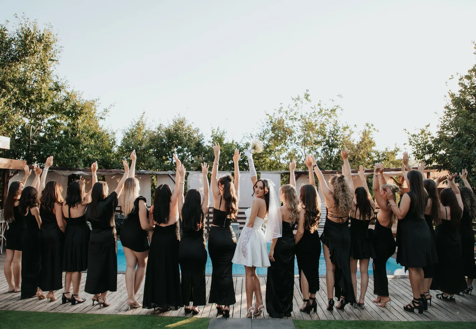 A bride in white celebrates with friends in black dresses at an outdoor bridal shower.