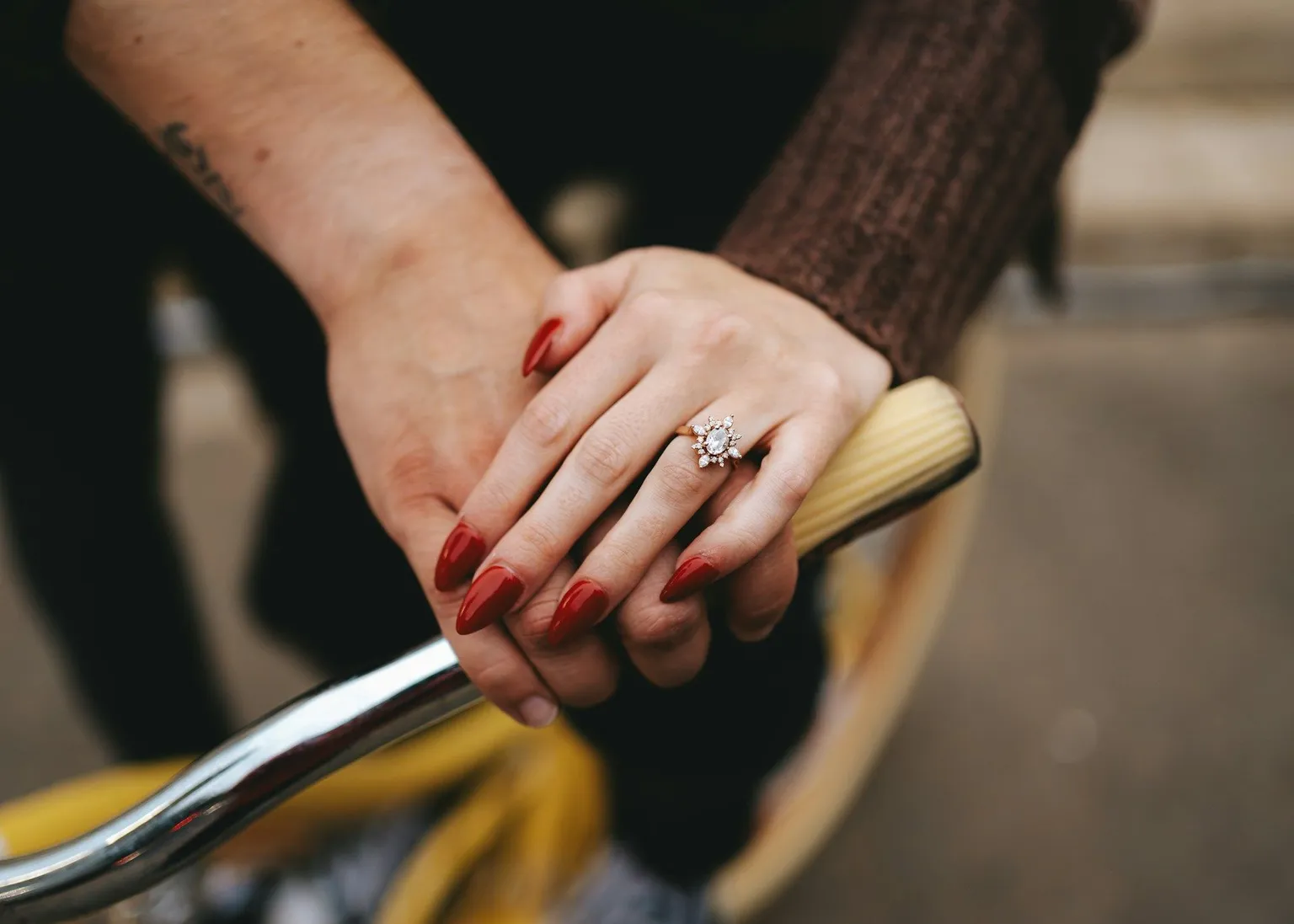 Close up of a hand with an engagement ring resting on a bicycle handle.