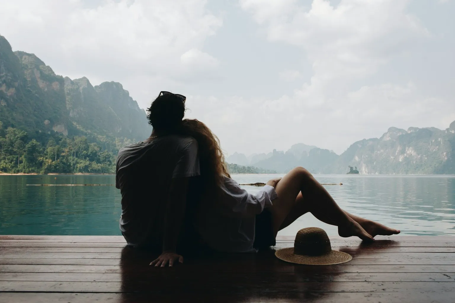 couple embracing while sitting on dock and looking out at water and mountains