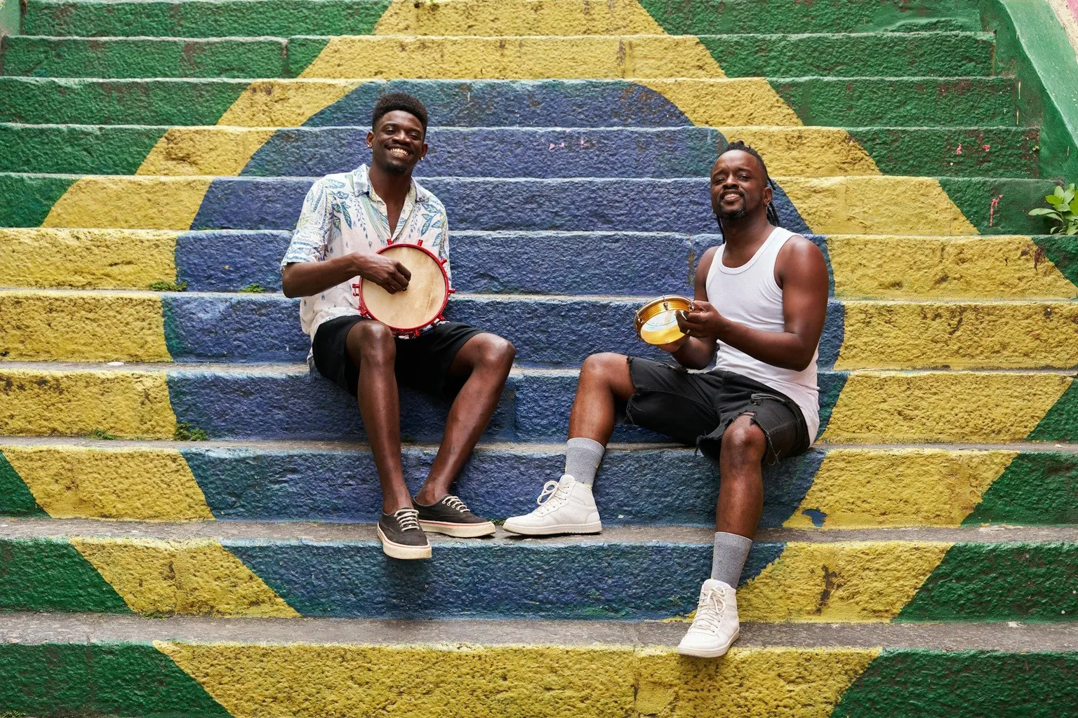 Two musicians playing pandeiro drums on stairs painted like the Brazilian flag in Rio.
