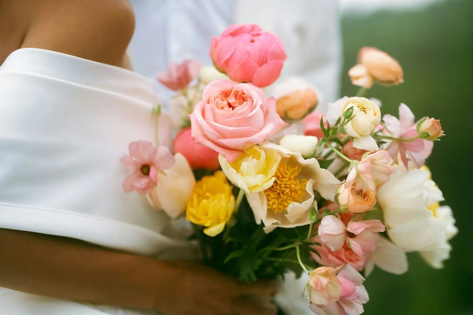 Soft pink, yellow, and white wedding bouquet held against the bride's dress.