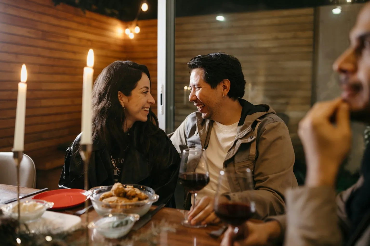 Friends laughing together at a candlelit dinner table.