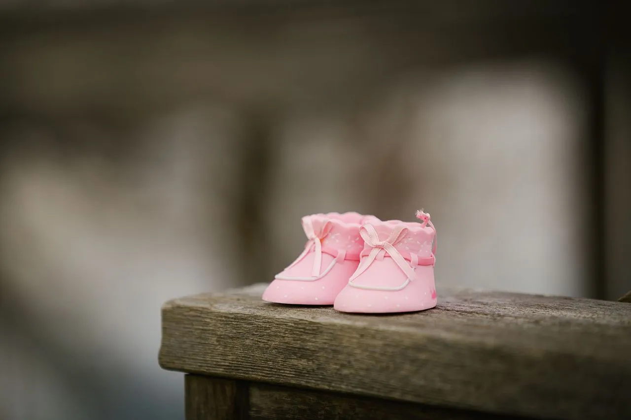 Pair of small pink baby shoes resting on a wooden surface.