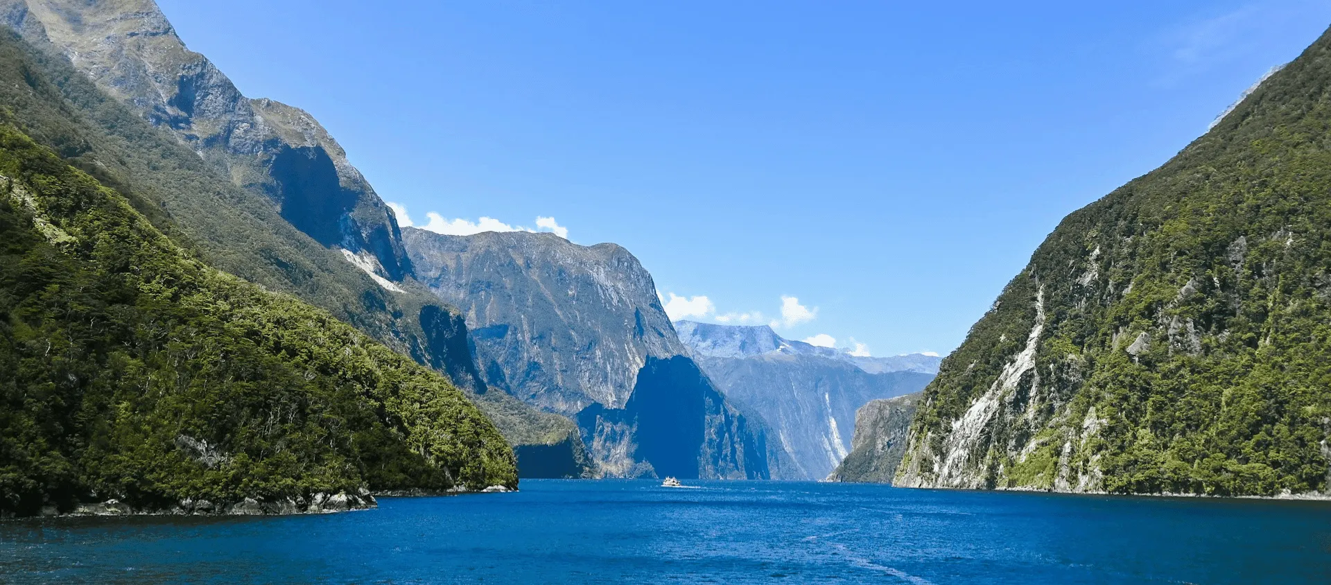 Blue water surrounded by steep green mountains under a clear sky.
