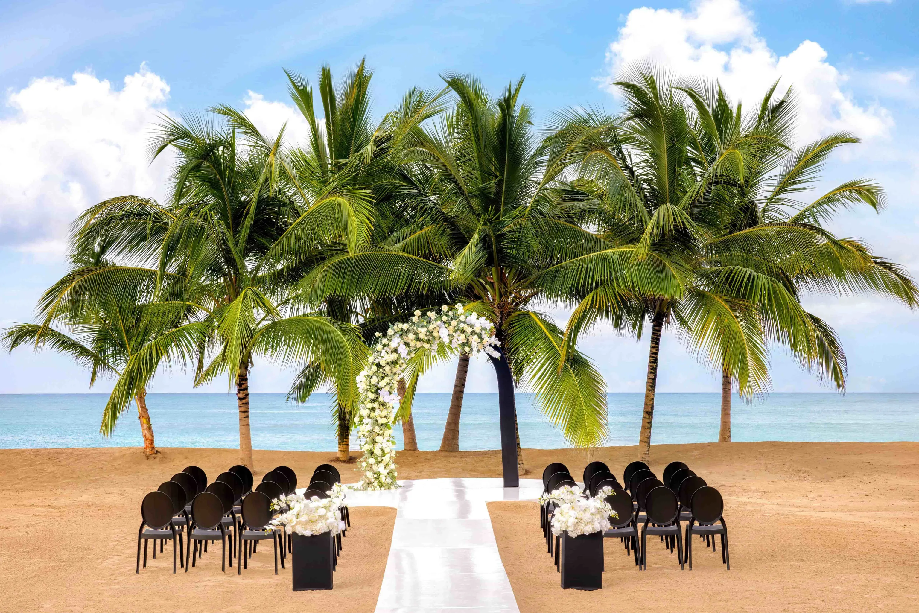 Beachfront wedding ceremony with a white floral arch and palm trees at Dreams Playa Esmeralda in Miches, Dominican Republic.