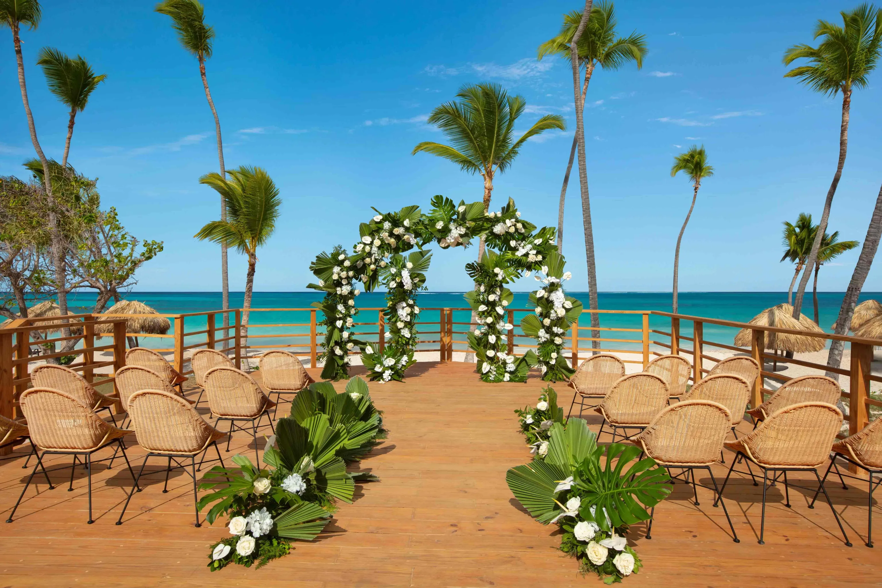 Oceanfront wedding ceremony arch with white flowers and chairs on a Caribbean beach deck.