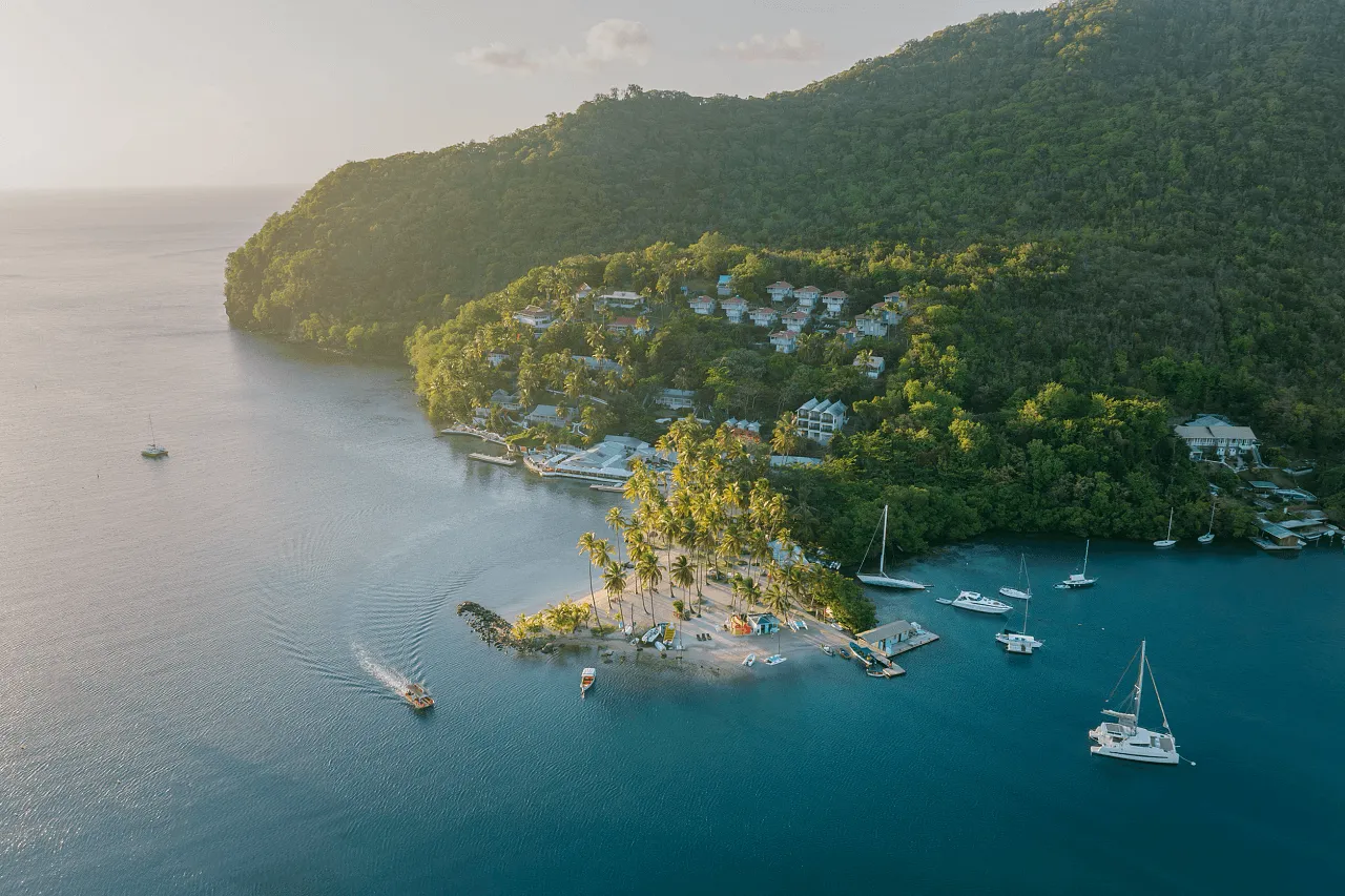boats riding around a peninsula on the ocean that has a resort and lush greenery