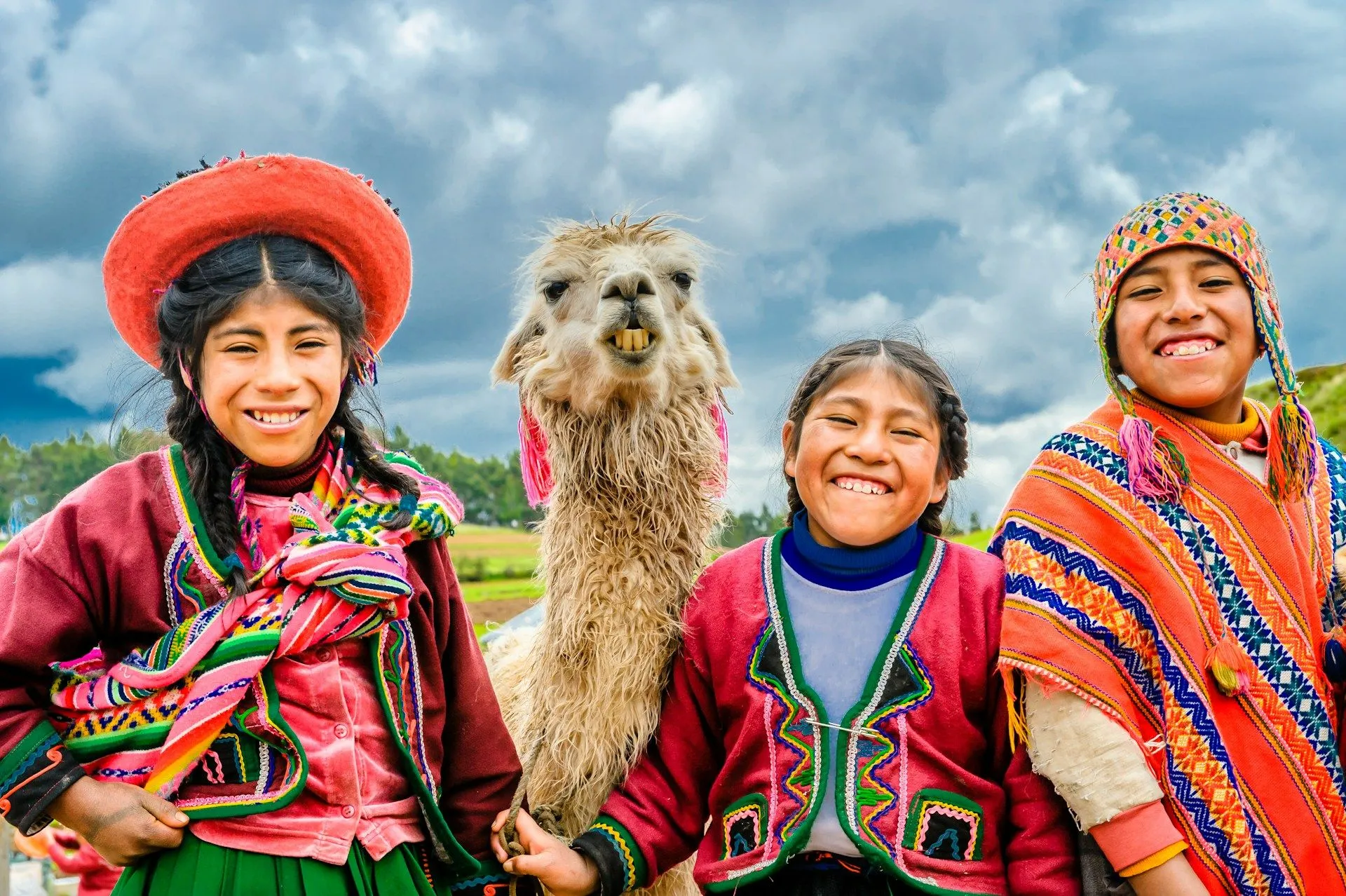 Three children in traditional Andean dress standing with a llama in Peru.