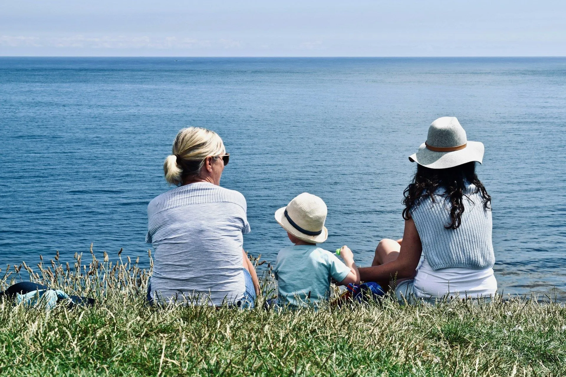 small child sitting on grass between two adults outlooking the ocean