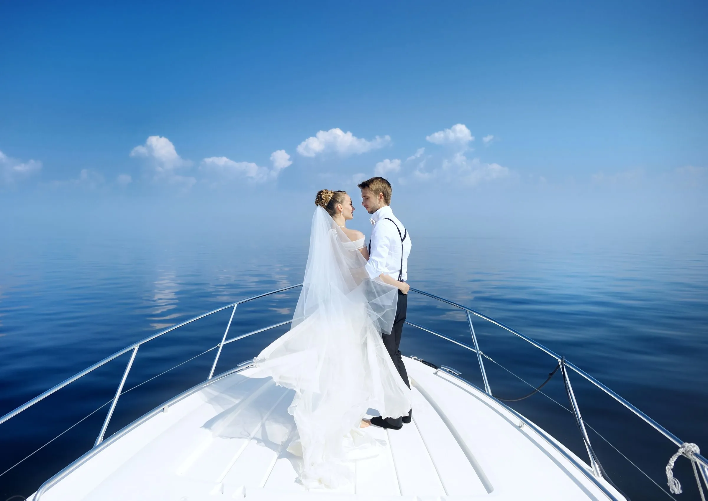 Bride and groom embrace on the bow of a boat surrounded by calm ocean waters.