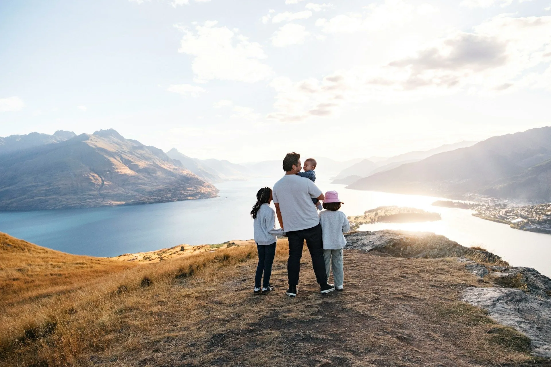 Family on a New Zealand road trip overlooking Lake Wakatipu and Queenstown at sunset