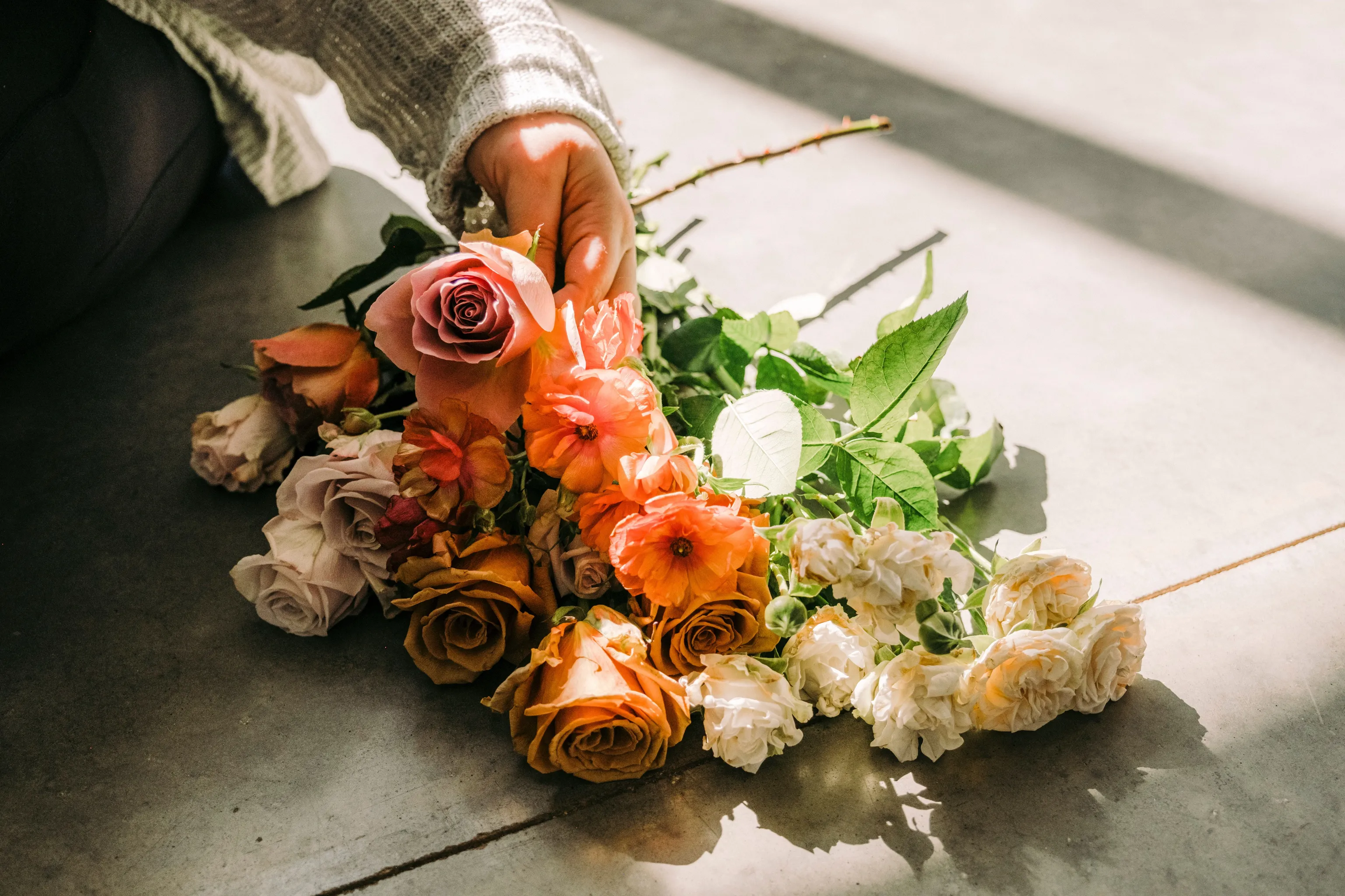 Hand placing a bouquet of flowers on a stone surface.