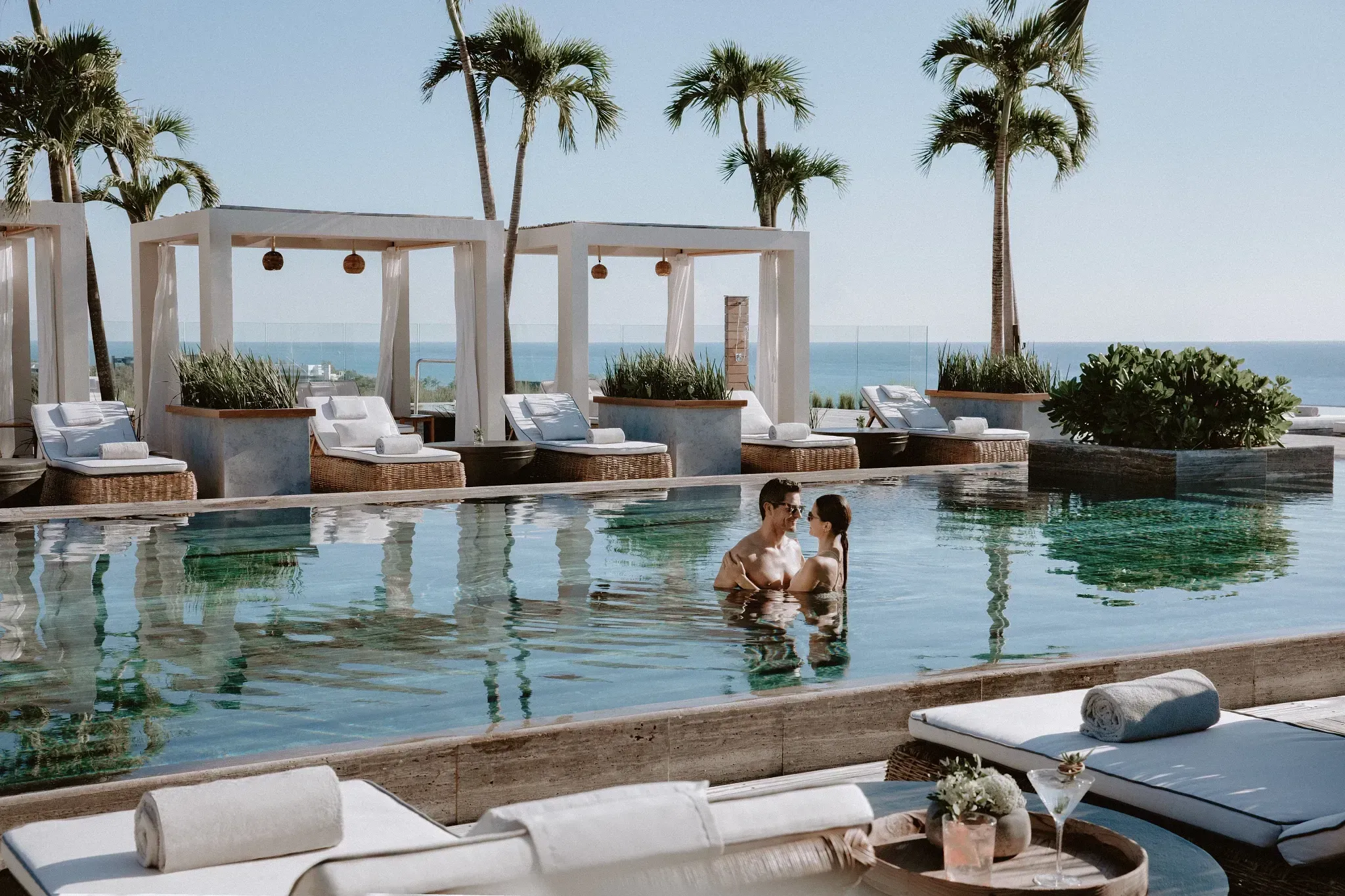 Couple relaxing in a resort pool with cabanas and palms.