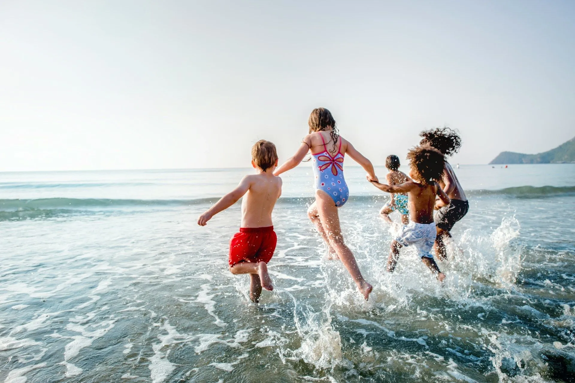Group of children running and splashing into the ocean at the beach.