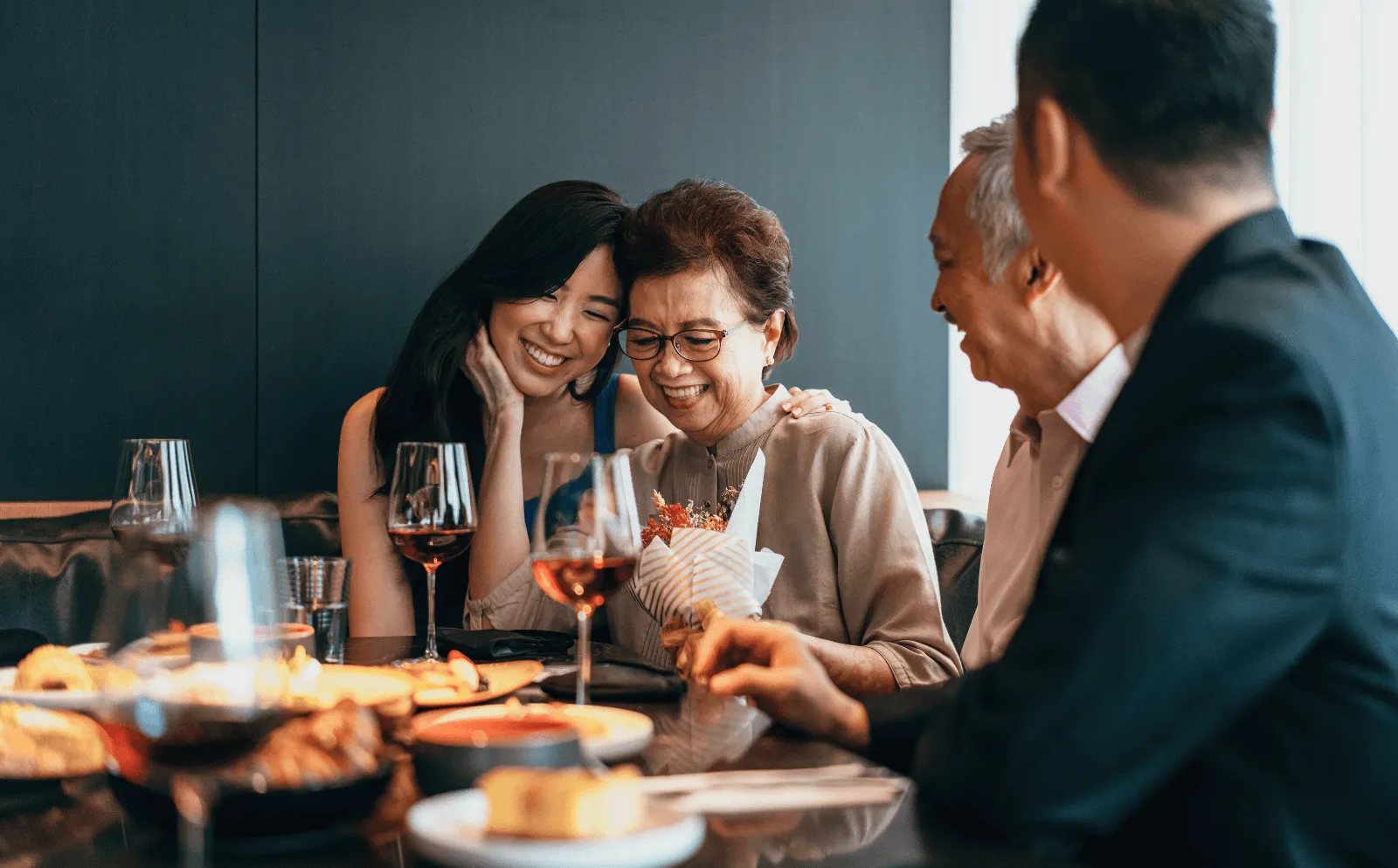 daughter and mother hugging while sitting at dinner table with family