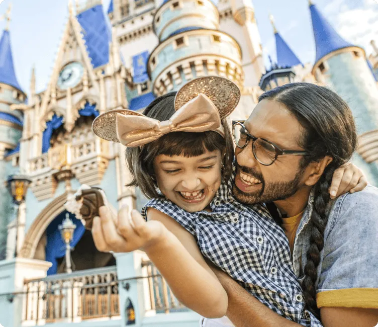 Parent and child laughing joyfully in front of Cinderella Castle