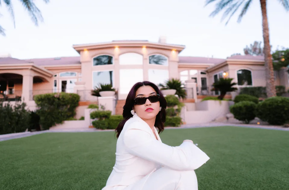 Stylish woman posing in front of a luxury home at sunset.