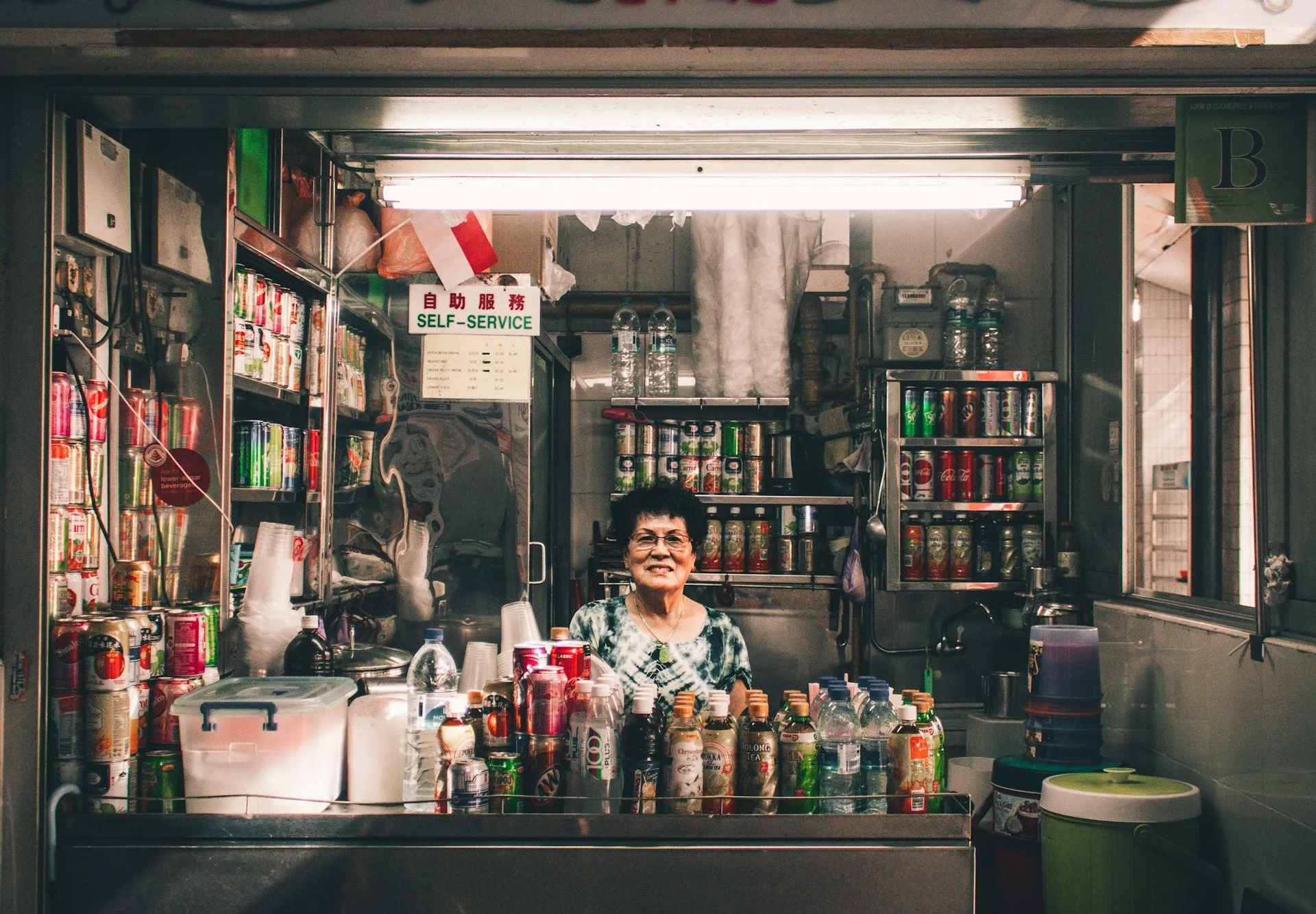 Hawker stall vendor smiling behind a counter stocked with drinks at a Singapore food centre