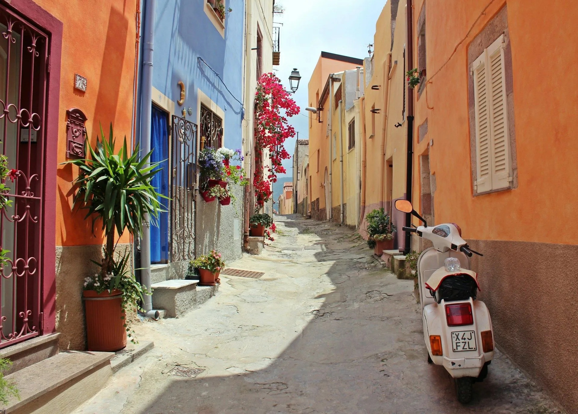 Narrow cobblestone street lined with colorful buildings and a parked white scooter.
