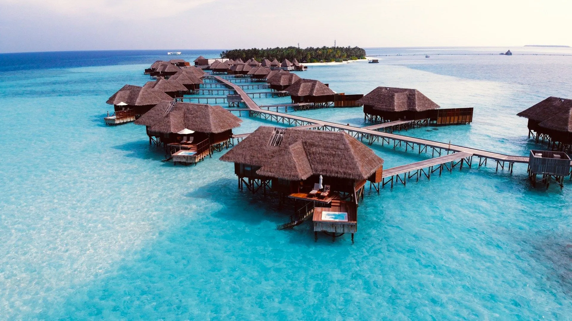 Luxury overwater villas on stilts surrounded by bright turquoise water at a tropical island resort.