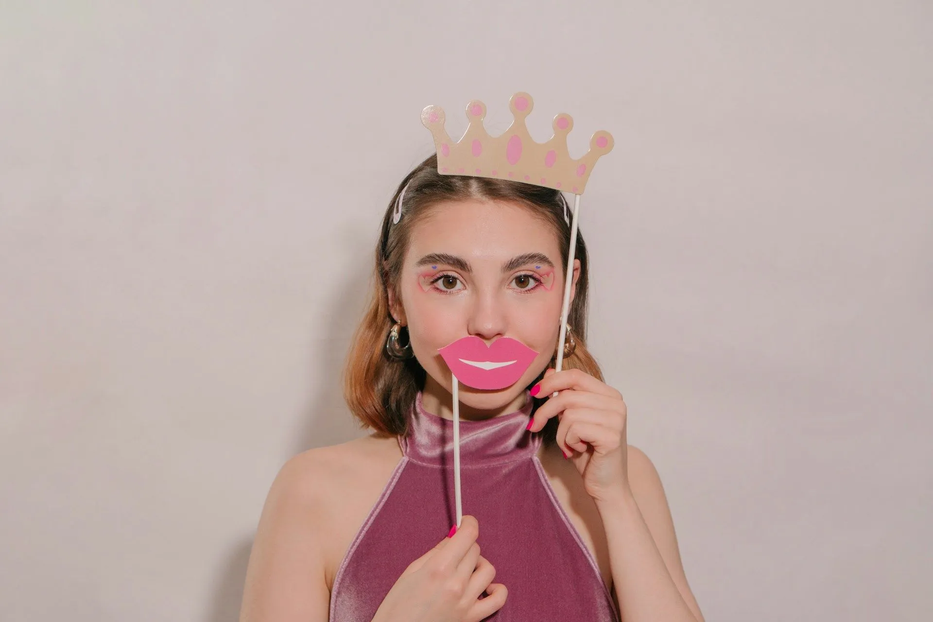 Person holding pink paper lips and a paper crown prop against a plain background.