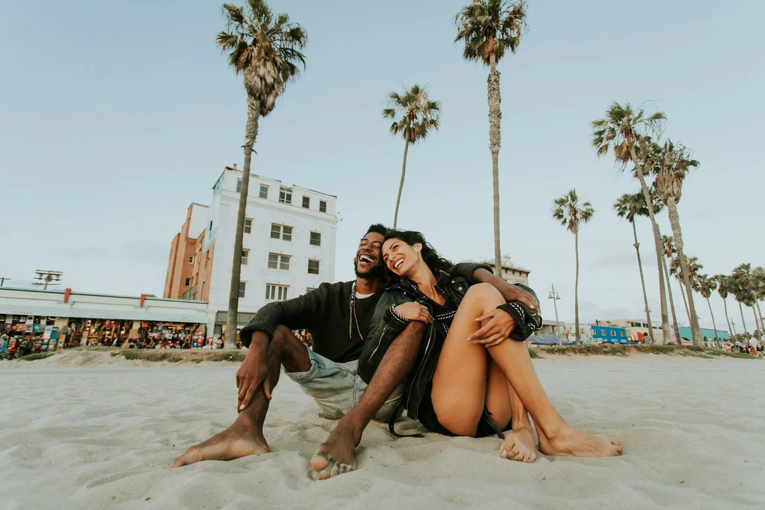 Couple relaxing on the sand at Venice Beach with palm trees in California.